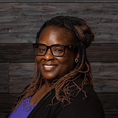 Chiropractor Sheryona Green-Owusu Smiling In Front Of Wooden Wall