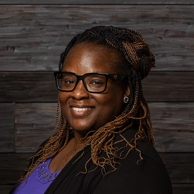 Chiropractor Sheryona Green-Owusu Smiling In Front Of Wooden Wall